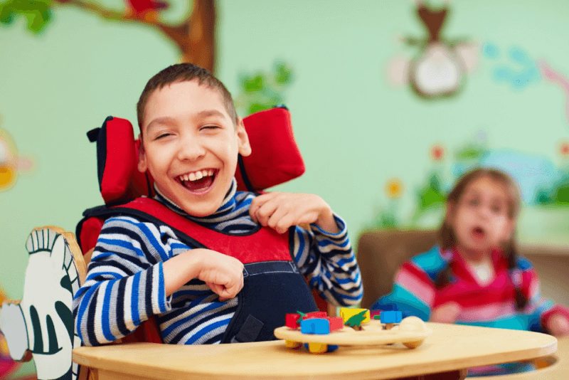 Male student with physical, cognitive disability smiling while working with a puzzle on a wheelchair tray